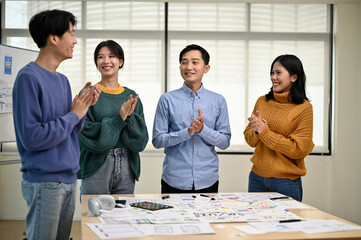 Wall Mural - A group of cheerful Asian developers is standing in the meeting, clapping their hands