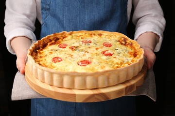 Woman with delicious homemade cheese quiche on black background, closeup