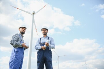 two engineers discussing against turbines on wind turbine farm.