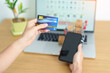 © Jo Panuwat D - woman hand holding credit card and using laptop with mobile phone for online shopping while making order. Marketplace platform website, technology, ecommerce, shipping delivery and online payment