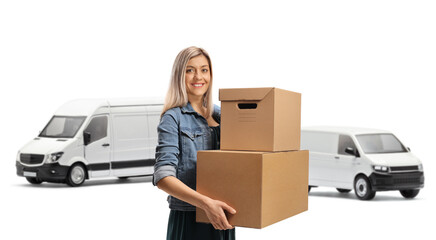 Wall Mural - Young cheerful woman carrying cardboard boxes amd standing in front of vans