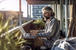 © Friedbert - A man sitting on a balcony using a laptop computer. Generative AI. Professional freelancer working from home, work life balance.