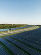 Autobahn zwischen Photovoltaik-Anlagen mit Windrädern im Hintergrund in grüner Natur bei Sonnenschein