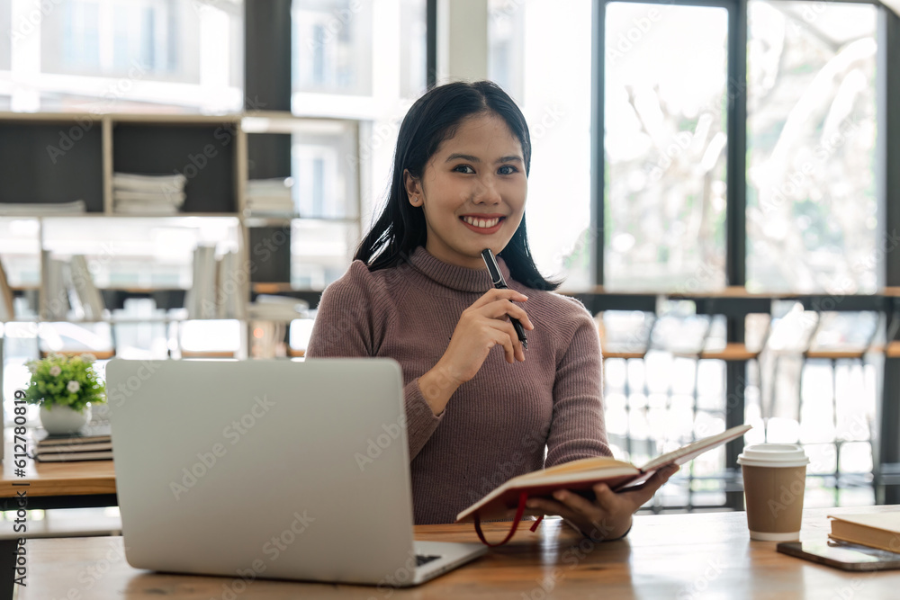 Asian student girl sitting at table looking book while do homework with ...