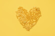 
heart made from different types of italian pasta on a yellow background. copy space.