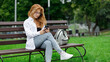 Young beautiful woman using her smartphone sitting on the bench in the park.