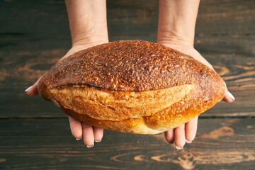 Wall Mural - Loaf of fresh made white bread in woman hands on wooden table background