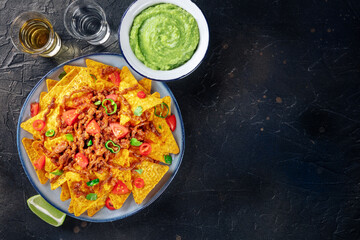 Nachos, Mexican food, tortilla chips with beef and fresh vegetables, overhead flat lay shot on a black background with tequila and guacamole