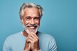 © Markus Schröder - Close-up portrait photography of a grinning mature man placing the hand over the mouth in a laughter gesture against a soft blue background. With generative AI technology