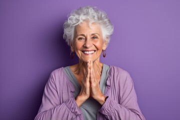 Canvas Print - Lifestyle portrait photography of a grinning mature woman making a heart with the hands against a lilac purple background. With generative AI technology