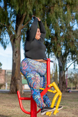 Wall Mural - Young fat woman doing leg exercise in the park by the lake. Healthy lifestyle