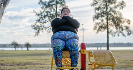 Wall Mural - Young fat woman doing abs workout in the park by the lake. Healthy lifestyle