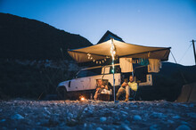 Man And Woman With Dogs Camping In Front Of A 4x4 Offroad Vehicle With Roof Tent At Night Time And Romantic Lighting On The Beach