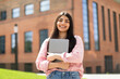 © Prostock-studio - Portrait of happy hispanic lady student posing with laptop in hands outdoors, looking and smiling at camera