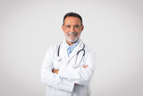 Fototapeta Na drzwi - Cheerful confident caucasian mature man doctor in white coat with crossed arms on chest looks at camera