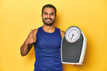 Poster - fit young latino man with scale on yellow background, fitness concept, smiling and raising thumb up