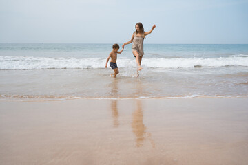 Wall Mural - Happy beautiful young mom plays with her son in sea waves