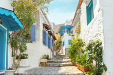 Narrow Street In Old European Town In Summer Sunny Day. Beautiful Scenic Old Ancient White Houses, Cafe And Shops With Pink Flowers. Popular Tourist Vacation Destination, Mediterranean Architecture