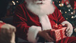 © wetzkaz - Santa Claus gives or wraps Christmas gifts, close-up hands, red Santa Claus costume, sits on a chair next to the decorated Christmas tree