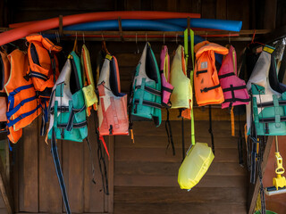 Multi-colored life jacket vests are hung on rail on wood wall for resort guests who want to do water activities, kayaking, stand-up paddleboarding, surfing and swimming, summer holiday travel concept.
