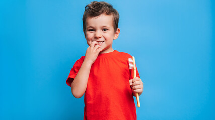 Wall Mural - Smiling boy with healthy teeth brushing his teeth with a toothbrush on a blue isolated background. Oral hygiene.