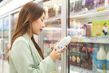 Asian Young Woman In Grocery, Supermarket Shopping Food Store Hand Holding Bottle Of Milk Or Yoghurt Take Out Of Refrigerator, Consumer Read Information On Label, Buying Healthy Dairy Products In Mall