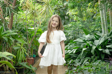 Little blonde girl in the botanical garden. a girl in a white dress exploring tropical plants and flowers in the greenhouse.