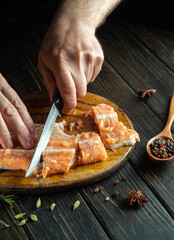 Male hands with a knife clean red fresh fish on a wooden cutting board. Home cooking of a delicious fish dish according to a unique recipe