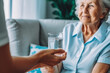 © VisualProduction - Nurse giving glass of water to elderly woman in wheelchair. Nursing home employee helping elderly people. Generative AI