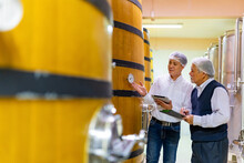 Professional Asian man winemaker working and inspecting wine quality in wine cellar with wooden barrel in wine factory. Winery manufacturing industry, Alcohol and winemaking fermentation process.