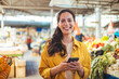 © Dragana Gordic - Woman at the farmer's market shopping, sending a text message on her smart phone. Young cheerful woman at the market. Smiling girl decided to cook a delicious and healthy meal