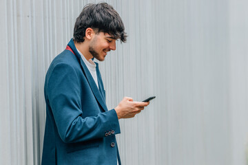 Wall Mural - young man or student in the street with mobile phone on the background wall