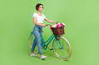Full size profile photo of cute positive girl fresh flowers basket bicycle walking empty space isolated on green color background