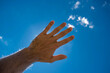 Ręka na tle niebieskiego nieba zasłaniająca słońce