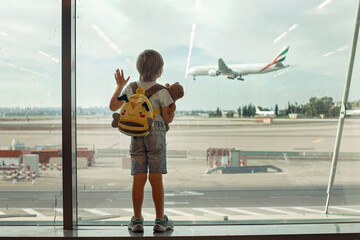 child, watching from the window of the airport the planes, taking off and landing while waiting at t