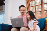 Fototapeta Tulipany - Cute little asian daughter with father working on laptop at home. single loving dad man shopping insurance to daughter by online technology.
