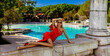 Glamour, stylish elegant woman in red long gown dress is posing need the pool in luxury hotel. Female model in amazing long dress. Outdoor shoot. Vogue. Couture.