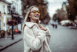 Portrait of a stylish fashion woman in yellow sunglasses and a fur coat in the city. Lifestyle