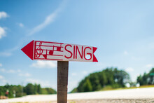 A Homemade Wooden Sign Reading "Sing" In Red Letters Along A Country Road, Closeup