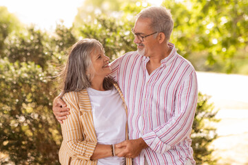 Wall Mural - Positive happy european mature couple hold hands, hugs, enjoy romantic date together in park at summer weekend