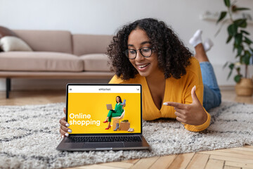 Happy black pointing at laptop computer screen with fashion store on screen, buying and ordering clothes at home
