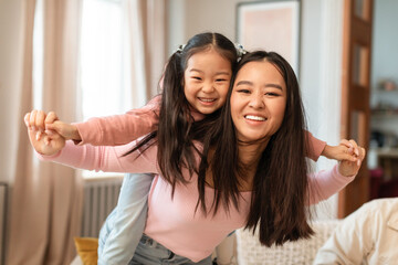 Wall Mural - Cheerful Asian Mom Carrying Daughter Piggyback Having Fun At Home