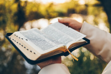 Poster - Christian woman holds bible in her hands. Reading the Holy Bible in a field during beautiful sunset. Concept for faith, spirituality and religion. Peace, hope