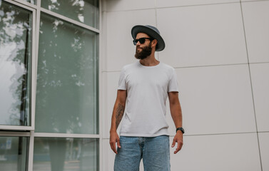 Wall Mural - City portrait of handsome hipster guy with beard wearing white blank t-shirt. Mock-up for print. T-shirt template.