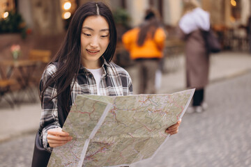 Portrait of a beautiful brunette Korean woman holding a map on the streets of the old city. Asian woman tourist or business lady traveling in Europe.