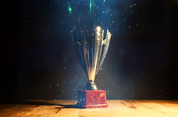 Wall Mural - low key image of trophy over wooden table and dark background, with abstract glitter lights