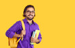 © Studio Romantic - Young positive Indian man student city college or university is holding books and backpack with educational supplies dressed in casual shirt stands in studio on yellow background