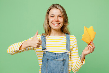 Wall Mural - Sick unhealthy ill allergic woman has red watery eyes runny stuffy sore nose suffer from allergy trigger symptom hay fever hold napkin show thumb up isolated on plain green background studio portrait