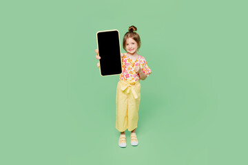 Wall Mural - Full body little child kid girl 6-7 years old wear casual clothes hold in hand use blank screen mobile cell phone isolated on plain pastel green background. Mother's Day love family lifestyle concept.