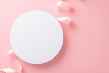 Top view photo of empty white circle with a pastel pink ribbon on an isolated light pink background with copyspace